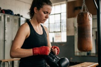 Femme se préparant pour sa première séance de boxe en salle en enfilant ses gants de boxe rouges dans un vestiaire de salle de sport