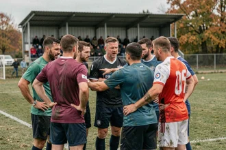 Joueurs de football amateur en cercle tactique sur un terrain de Fédérale 2, saison 2026