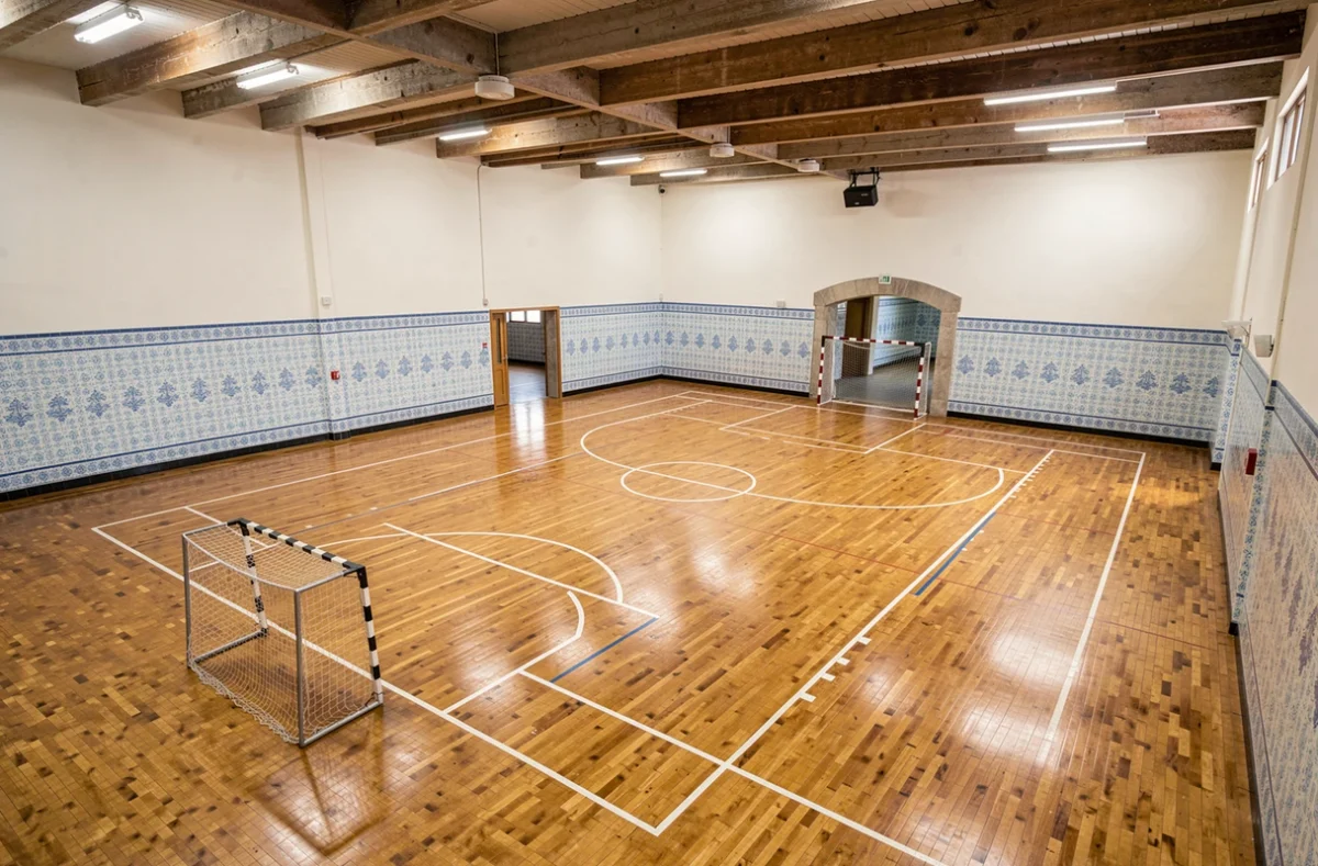 Terrain de handball vide dans une salle municipale portugaise, vue en plongée montrant les buts, les lignes peintes et le parquet brillant avec des détails architecturaux typiques du Portugal